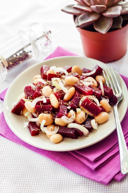 Insalata di barbabietola con fagioli bianchi, sottaceti e cipolla, condita con olio e aromatizzata con semi di cumino