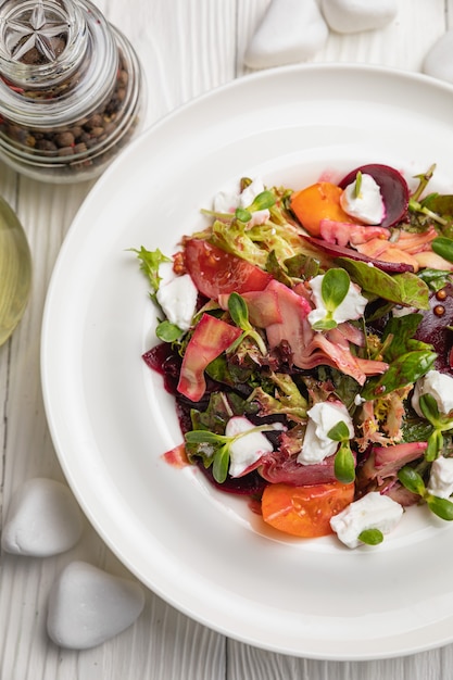 Insalata di barbabietole formaggio pomodori e verdure su un piatto bianco e un tavolo bianco