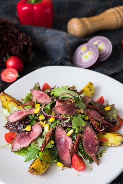 Insalata di carne calda con rucola sul piatto bianco su sfondo di pietra scura.