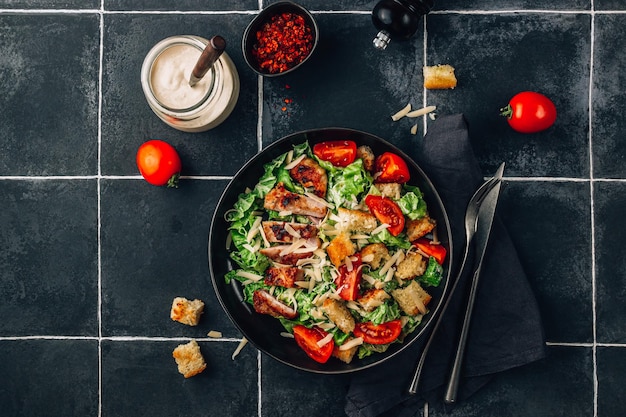 Insalata di Cesare fatta in casa con pollo croccante e pomodori su uno sfondo di piastrelle nere