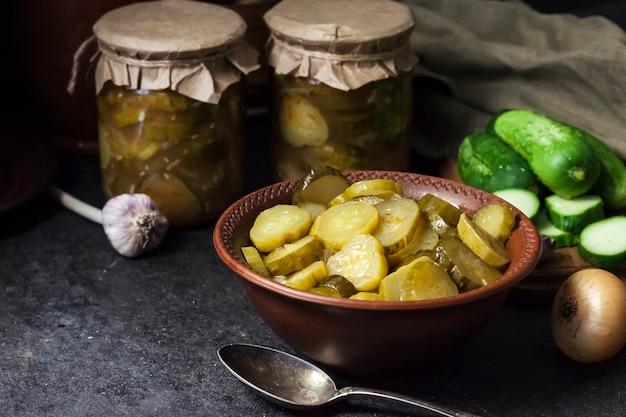 Insalata di cetrioli sottaceto in una ciotola e barattoli su sfondo nero