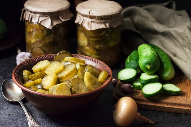 Insalata di cetrioli sottaceto in una ciotola e barattoli su sfondo nero