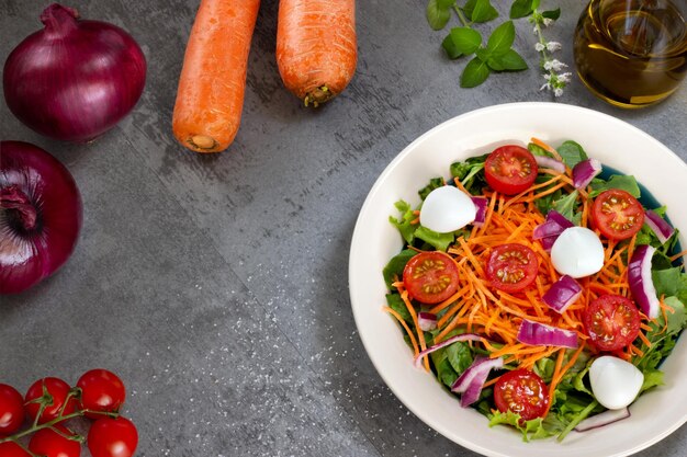 Insalata di foglie verdi su tavola grigia con olio d'oliva foglie di basilico carote cipolle rosse e pomodori vista dall'alto