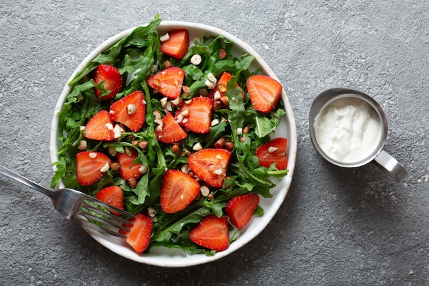 Insalata di fragole con rucola su un piatto con una forchetta su sfondo grigio chiaro