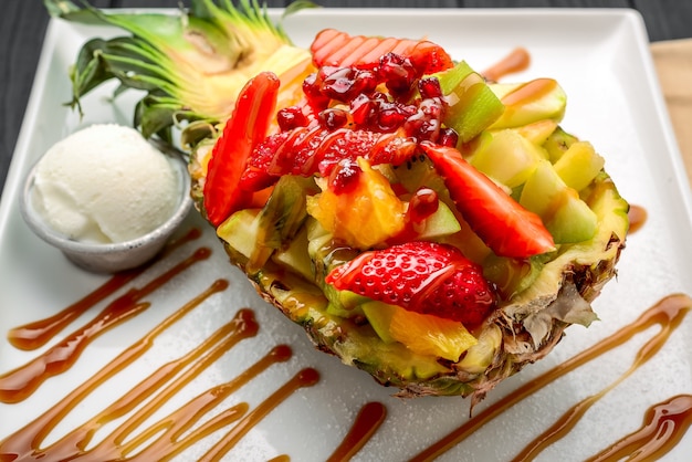 Insalata di frutta fresca in ananas tagliato a metà, versata con caramello