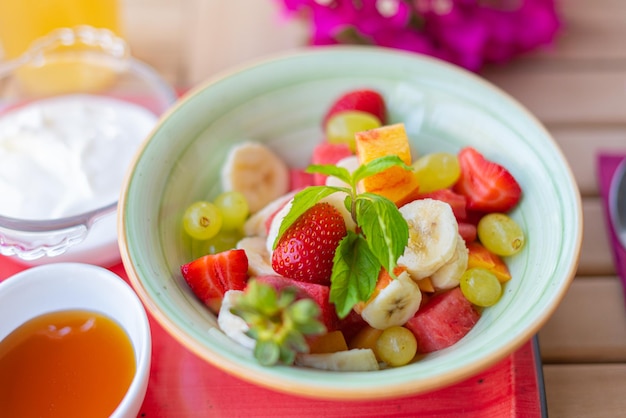 Insalata di frutta fresca sana sul tavolo della colazione. Macedonia di frutta in ciotola con miele e yogurt greco.