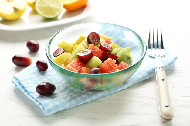 Insalata di frutta in ciotola di vetro su fondo di legno chiaro