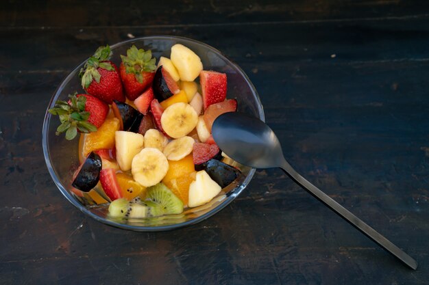 Insalata di frutta sana e naturale con arancia in una ciotola di vetro trasparente, su una superficie nera rustica.