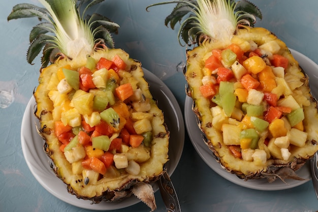 Insalata di frutta tropicale a metà ananas su uno sfondo azzurro, primo piano, vista dall'alto