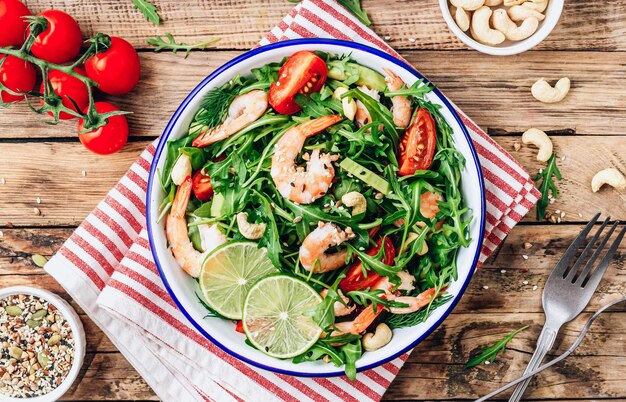 Insalata di gamberetti fatta in casa con pomodoro, rucola, avocado e anacardi su sfondo rustico in legno Vista dall'alto