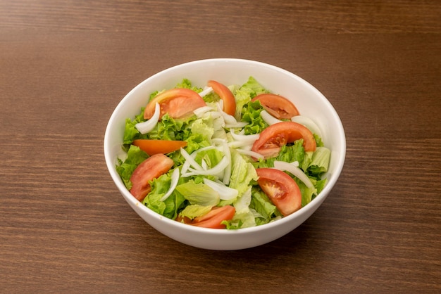 Insalata di giardino con lattuga di pomodoro tritata e cipolla bianca croccante in una semplice ciotola bianca e tavolo di legno