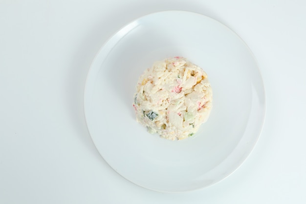 Insalata di granchio con riso sul primo piano bianco del piatto con lo spazio della copia. Insalata tradizionale russa con bastoncini di granchio isolati su bianco