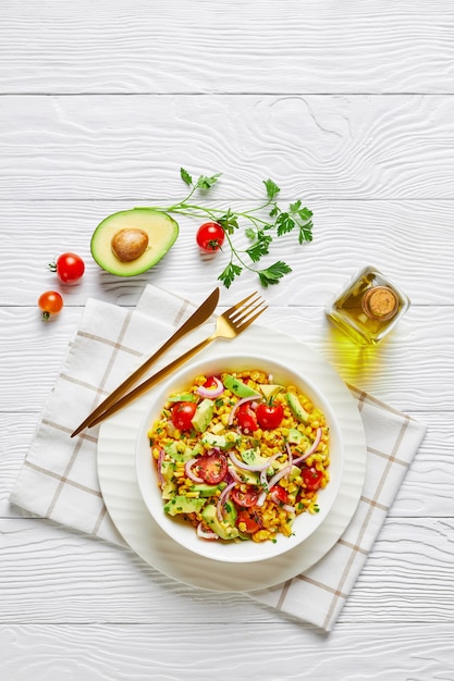 Insalata di mais dolce con avocado, fette di cipolla rossa e pomodori in una ciotola bianca su un tavolo di legno, cucina messicana, vista orizzontale dall'alto, piatto, spazio libero