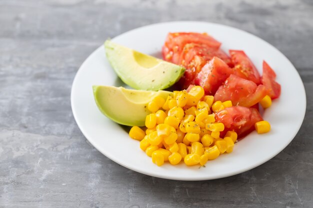 Insalata di mais, pomodoro e avocado sul piatto bianco su fondo in ceramica