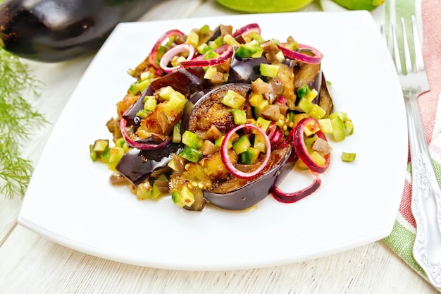 Insalata di melanzane fritte fresche e cetrioli sottaceto con cipolla rossa condita con olio vegetale e salsa piccante in un piatto asciugamano forchetta e aneto su uno sfondo di tavola di legno