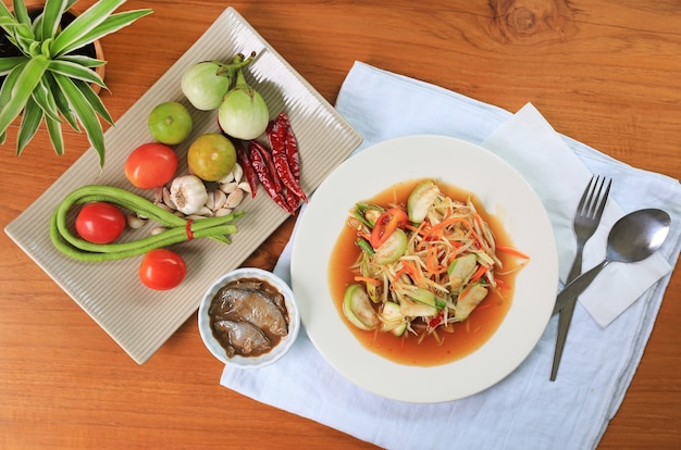 Insalata di papaia verde con pesce in salamoia sul piatto bianco contro il fondo della tavola in legno. Vista dall'alto