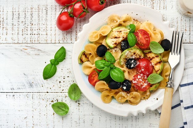 Insalata di pasta fiocchi con verdure zucchine grigliate, pomodorini, olive, basilico e parmigiano in piastra bianca su sfondo chiaro di ardesia, pietra o cemento. Concetto di pranzo. Vista dall'alto.