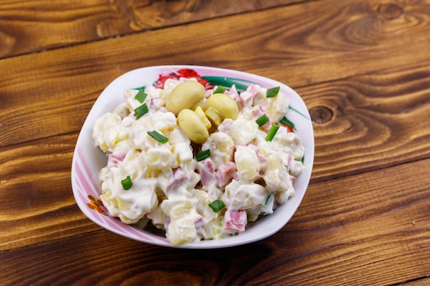 Insalata di patate con funghi marinati, salsiccia, cipolla e maionese su tavola di legno