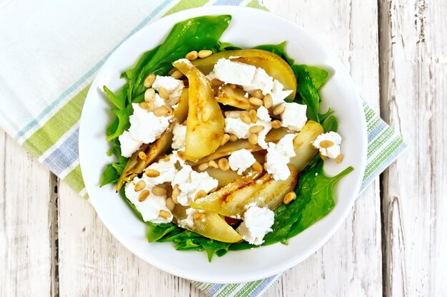 Insalata di pere fritte, spinaci, feta salata e noci di cedro in un piatto su un tovagliolo su una tavola di legno sfondo dall'alto