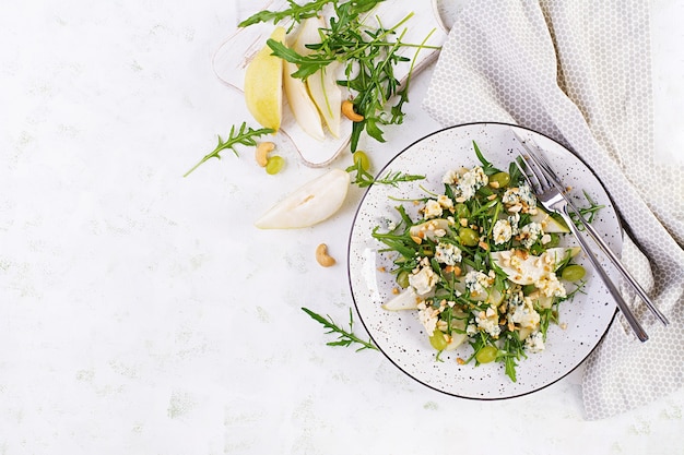 Insalata di pere, gorgonzola, uva, rucola e noci con salsa piccante su sfondo chiaro. Mangiare sano. Vista dall'alto, dall'alto