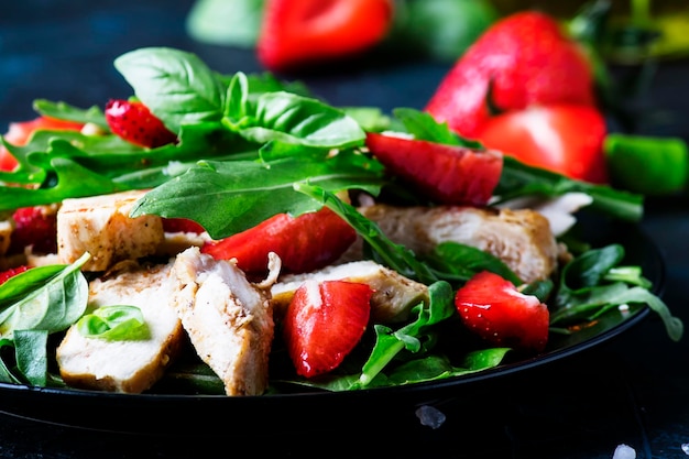 Insalata di pollo alla griglia fragole fresche e rucola piccante sfondo scuro fuoco selettivo