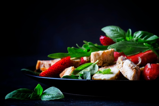 Insalata di pollo alla griglia fragole fresche e rucola piccante sfondo scuro fuoco selettivo