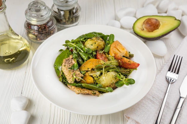 Insalata di pollo alla griglia pomodori patate e verdure su un piatto bianco e un tavolo bianco