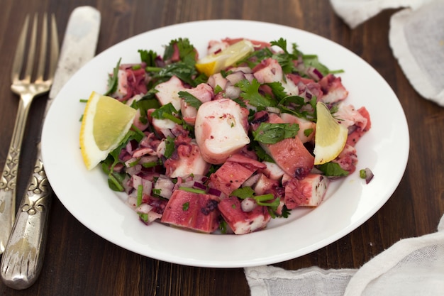 Insalata di polpo con limone sul piatto bianco su superficie di legno