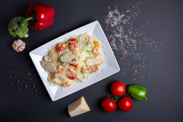 Insalata di pomodori, briciole, cavoli, gamberi e formaggio, su fondo nero con pomodori, aglio, peperoni verdi rossi e broccoli