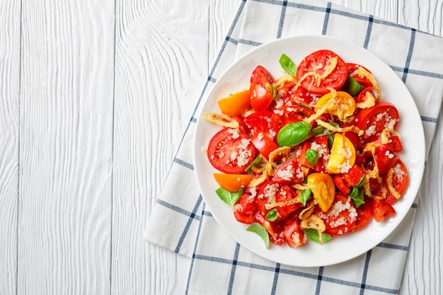 Insalata di pomodori con cipolla fritta croccante, quinoa e basilico fresco su un piatto bianco su un tavolo di legno, primo piano, vista del paesaggio dall'alto, piatto, spazio libero