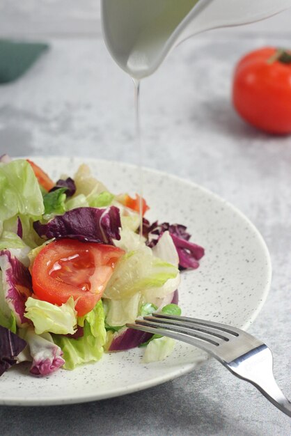 Insalata di pomodoro e lattuga in un piatto sul tavolo Olio che versa dall'alto