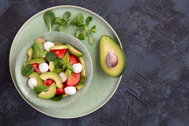 Insalata di pomodoro mozzarella avocado basilico su sfondo scuro da tavola Mangiare sano cibo vegetariano