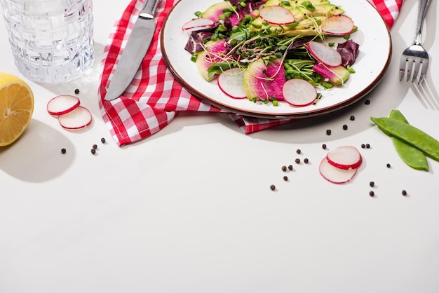 Insalata di ravanello fresco con verdure e avocado su piatto su superficie bianca con acqua e posate