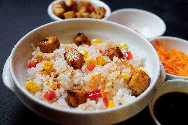 Insalata di riso vegetariana con tofu e riso integrale su sfondo nero.