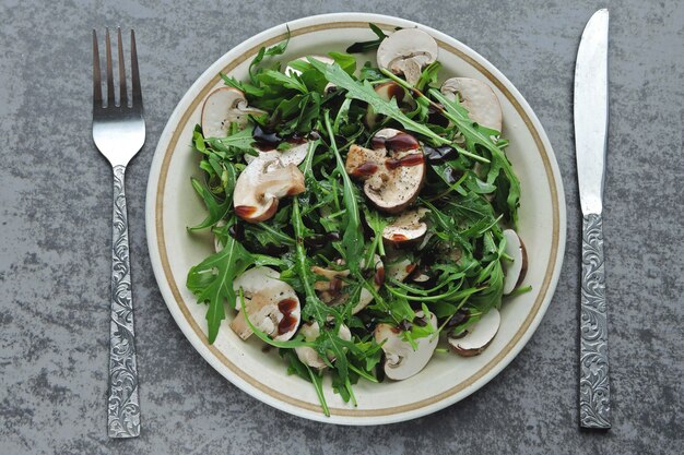 Insalata di rucola sana con funghi prataioli crudi con olio d'oliva e salsa di soia Insalata vegana con funghi crudi.