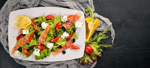 Insalata di salmone foglie di insalata di formaggio feta e verdure fresche sul piatto Su uno sfondo di legno Vista dall'alto Spazio libero per il testo