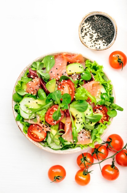 Insalata di salmone fresco con avocado cetriolo semi di sesamo olio d'oliva pomodori ed erbe miste Sfondo bianco vista dall'alto