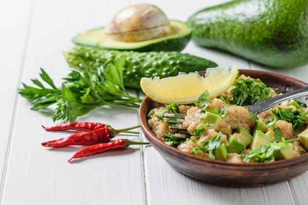 Insalata di semi di amaranto, avocado, pepe, limone e prezzemolo con olio d'oliva su un tavolo di legno bianco.