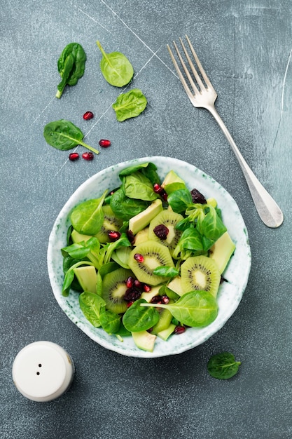 Insalata di spinaci baby foglie, crescione, kiwi, avocado e melograno in un vecchio piatto di ceramica su una superficie di cemento grigio