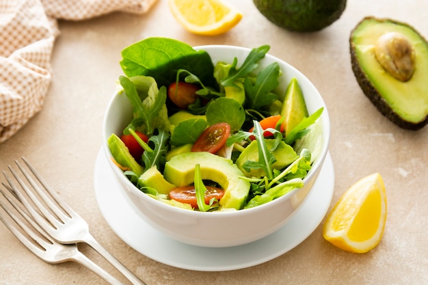 insalata di spinaci di avocado con succo di limone in una ciotola con due forchette su sfondo chiaro