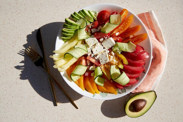 Insalata di stagione sana con arancia rossa e pomodori gialli peperoni avocado cetrioli formaggio feta sesamo sotto ombre dure Alimenti biologici naturali corretta alimentazione