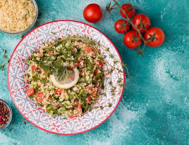 Insalata di taboule orientale tradizionale su uno sfondo blu accanto agli ingredienti.