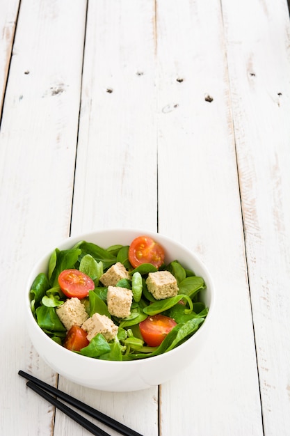 Insalata di tofu vegano con pomodori e lattuga di agnello sul tavolo di legno bianco