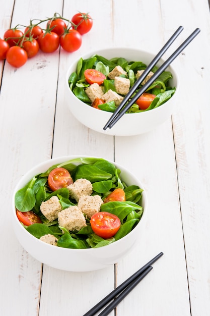 Insalata di tofu vegano con pomodori e lattuga di agnello sul tavolo di legno bianco