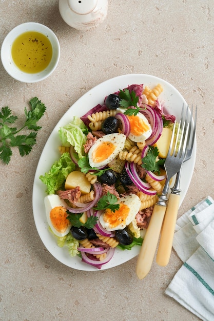 Insalata di tonno con pasta uova patate olive cipolle rosse e salsa in piatto bianco su vecchio sfondo tavolo in cemento grigio chiaro Insalata nizzarda Cucina francese Vista dall'alto Posa piatta