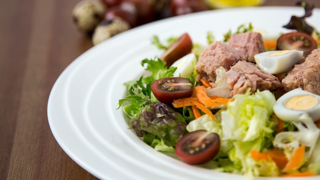 Insalata di tonno fresca e leggera con lattuga, uova e pomodori Verdure tritate Cibo sano per la vita su fondo in legno Luce naturale Messa a fuoco selettiva