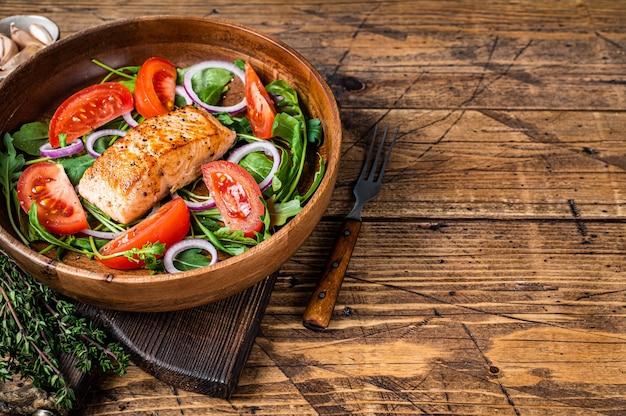 Insalata di trancio di salmone con foglie verdi di rucola, avocado e pomodoro in un piatto di legno