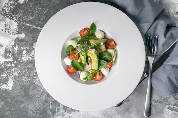 Insalata di verdure con avocado, mozzarella, pomodorini e erbe su un grande piatto bianco.