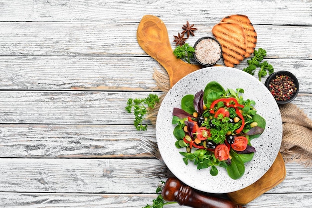 Insalata di verdure con spinaci, pomodori, paprika e semi di zucca in un piatto su fondo di legno Vista dall'alto. Spazio libero per il tuo testo. Disposizione piatta