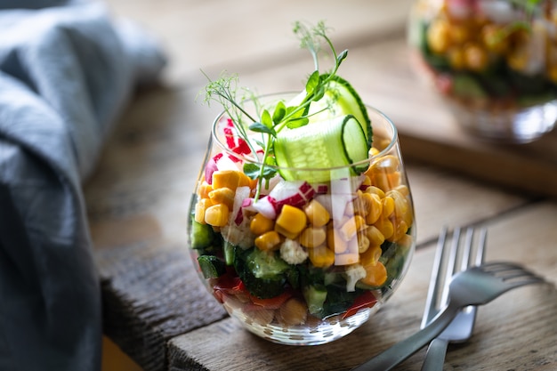 Insalata di verdure della primavera in una tazza di vetro su un fondo di legno. Nutrizione appropriata. Copia spazio. Verticale. Messa a fuoco selettiva.